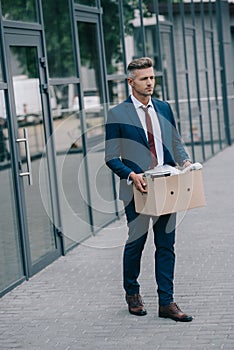 Businessman walking near building and holding carton box