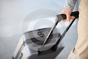 Businessman walking outside public transport building with luggage in rush hour. Business traveler pulling suitcase in modern airp