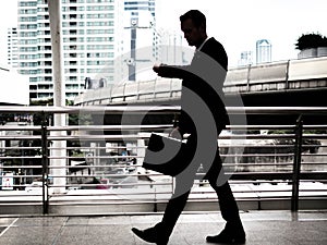 Businessman walking on the skywalk hastily. In his hand is a black leather briefcase. with flare light