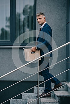 Businessman walking on stairs near building and holding carton box