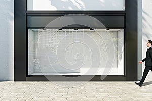 Businessman walking through sunlit empty showcase with light wall background behind window with space for product presentation in