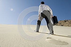 Businessman Walking Uphill In Desert