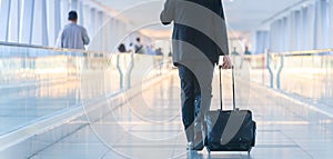 Businessman walking and wheeling a trolley suitcase at the lobby, talking on a mobile phone. Business travel concept.