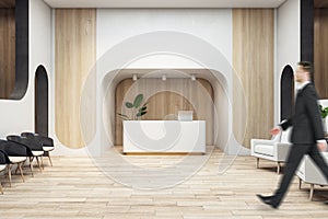 Businessman walking in wooden office interior with reception desk. Waiting area, worker and lobby concept