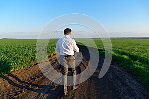 Businessman walks along a country road, green field, freelance and business concept, green grass and blue sky as background