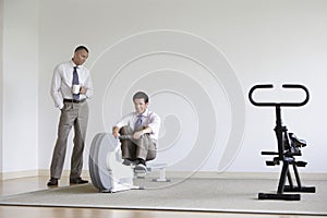 Businessman Watching Colleague Use Rowing Machine