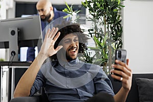 Businessman waving hi while talking on smartphone online meeting