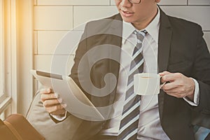 Businessman wearing black suit sitting and reading news in tablet computern