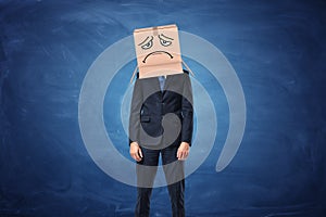 Businessman wearing cardboard box with drawn sad face on his head