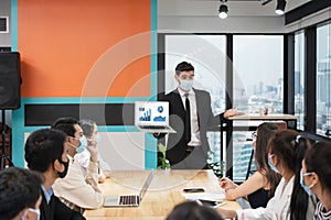 Businessman wearing face mask with presentation of business plan on laptop, corporate business meeting in modern office