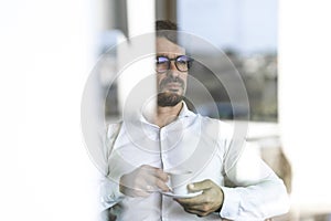 Businessman wearing glasses sitting down drinking an expresso coffee