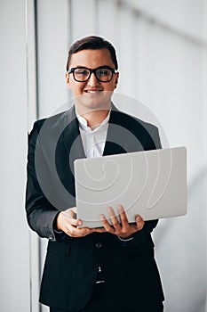 Businessman wearing glasses and suit working laptop holding hands near panoramic window.