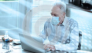 Businessman wearing medical face mask and working on laptop from home; light effect