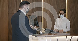 Businessman wearing medical mask talking to hotel manager at reception desk during pandemic
