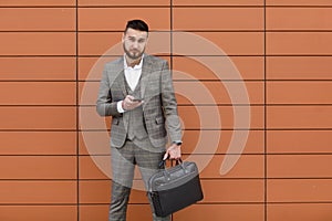 Businessman wearing suit and using modern smartphone near office at early morning, successful employer to make a deal