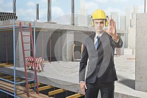 Businessman wearing yellow safety helmet and showing stop gesture at construction site