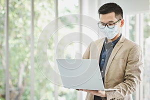 Businessman wears face mask standing and holding laptop