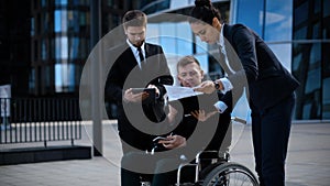 Businessman in a wheelchair with colleagues outside an office building discuss abut deal and business.
