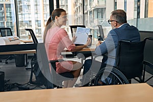 Businessman in wheelchair and friendly company employee adjust working papers