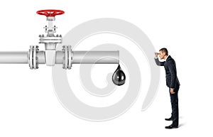 Businessman on white background looking at pipe with red valve that`s leaking one big oil drop