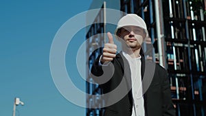 businessman in a white helmet, in a suit, holding a project in his hand, against the backdrop of a skyscraper