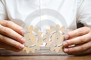 Businessman in white shirt connects two wooden gears. Symbolism of establishing business processes and communication. Improving