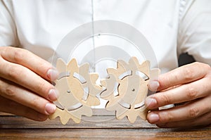 Businessman in white shirt connects two wooden gears. Symbolism of establishing business processes and communication. Improving photo