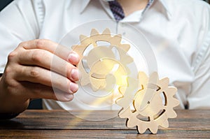 Businessman in white shirt connects two wooden gears. Symbolism of establishing business processes and communication. Increase