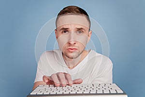 Businessman in white t-shirt typing on computer keyboard email work focused isolated over blue color background