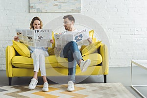 Businessman with wife reading newspapers about travel and business while sitting on sofa in modern room