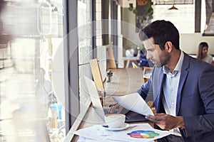 Businessman By Window Working On Laptop In Coffee Shop