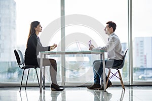 Businessman and woman having a discussion in the office face to face at table against windows