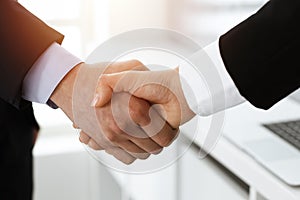 Businessman and woman shaking hands in sunny office, close-up. Concept of handshake as success symbol in business