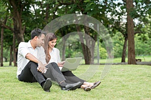 Businessman and woman use laptop in park