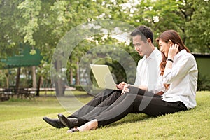 Businessman and woman use laptop in park, sit on grass together