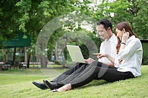 Businessman and woman use laptop in park, sit on grass together