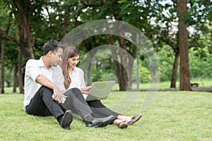 Businessman and woman use laptop in park, sit on grass together