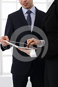 Businessman and woman using tablet computer for discussing questions in office. Partners or colleagues at meeting