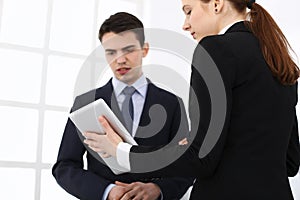 Businessman and woman using tablet computer for discussing questions in office. Partners or colleagues at meeting