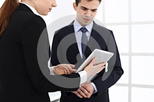 Businessman and woman using tablet computer for discussing questions in office. Partners or colleagues at meeting