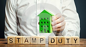 Businessman and wooden blocks with the word Stamp duty and house. Taxes assessed during the transfer of real estate between two photo