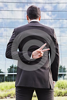 Businessman or worker in suit shows peace sign near office building