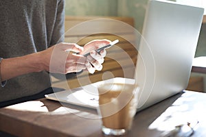 Businessman working alone on laptop and using mobile smartphone in sunny cafe, having coffee. Focus on manâ€™s hands