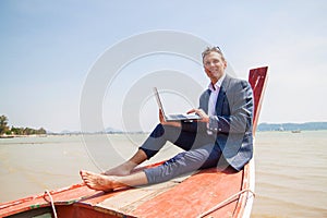 Businessman working with computer on a boat, nice outdoor office.