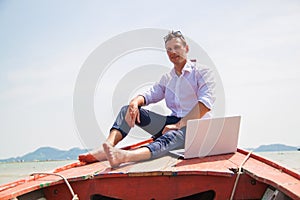 Businessman working with computer on a boat, nice outdoor office.