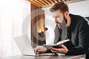 Businessman is working on computer, holding notepad. Man typing on laptop, looking webinar, analyzes information, data.