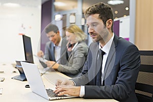 Businessman working on computer in modern office, colleagues in