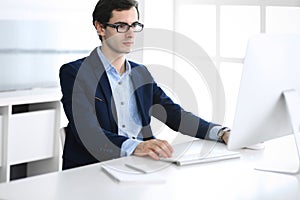 Businessman working with computer in modern office. Headshot of male entrepreneur or company manager at workplace