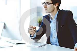 Businessman working with computer in modern office. Headshot of male entrepreneur or company manager at workplace