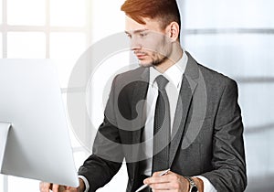 Businessman working with computer in sunny office. Headshot of male entrepreneur at workplace. Business concept